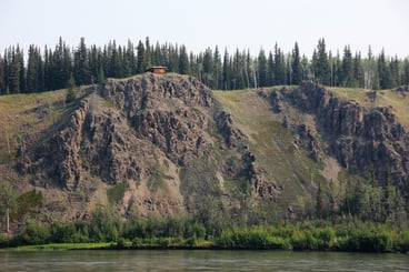 Cabin on a cliff with forest and water.